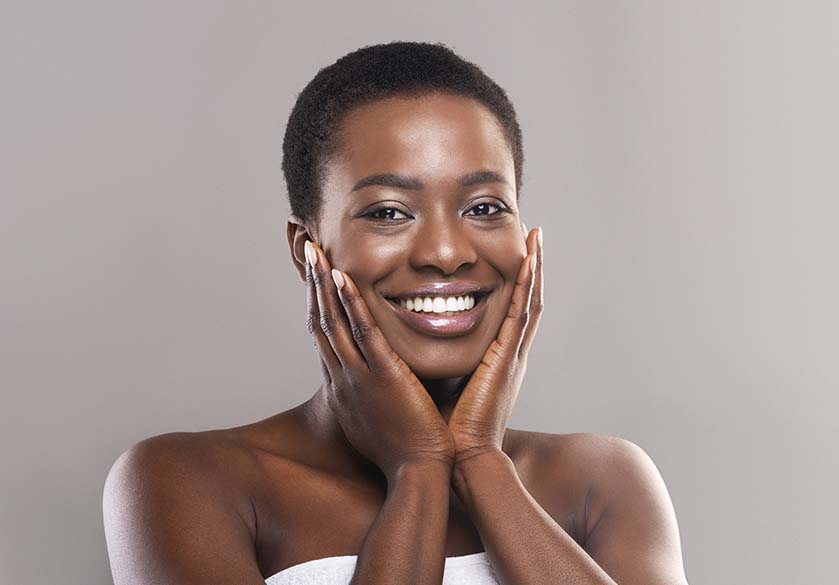 Beautiful afro woman with short hair touching face with perfect smooth skin, grey background